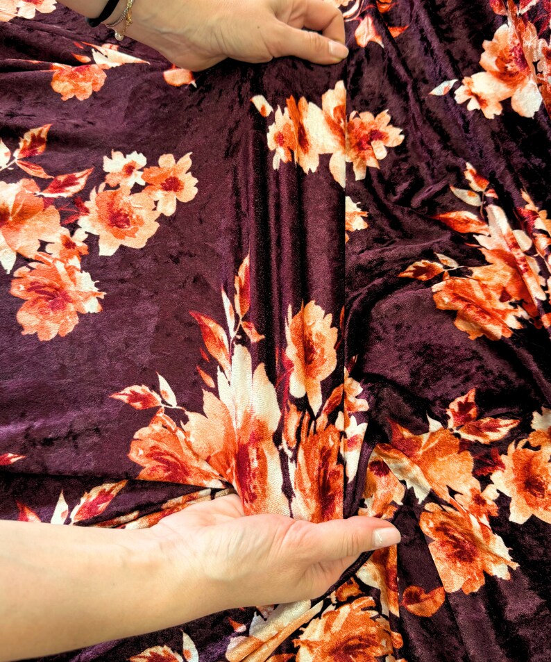 May include: Burgundy velvet fabric with a floral print in shades of orange and white. The fabric is soft and has a subtle sheen.
