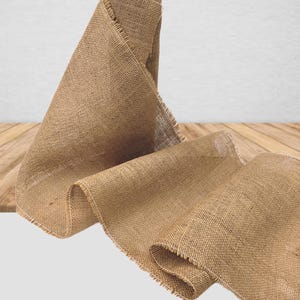 May include: A roll of natural brown burlap fabric with frayed edges. The fabric is woven with a loose, open weave and has a rustic, natural look.