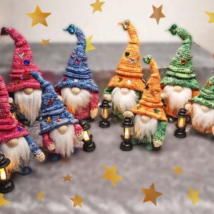 Può includere: Una collezione di figurine di gnomi fatti a mano con lunghe barbe bianche e cappelli a punta colorati. Ogni gnomo tiene in mano una piccola lanterna. I cappelli sono in tonalità di rosa, blu, arancione e verde, decorati con stelle e gemme. Decorazioni a stella dorata sullo sfondo.