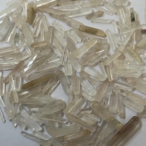 May include: A collection of small, clear, and translucent crystal shards. The crystals vary in size and shape, with some appearing more elongated and others more rounded. The color ranges from clear to a pale, milky white, with some having a slight amber hue.