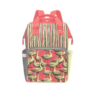 May include: A multi-pocket backpack with a red and cream striped top section and a lower section featuring a pattern of geese on a red background. The backpack has a gray side pocket and a red handle and straps.