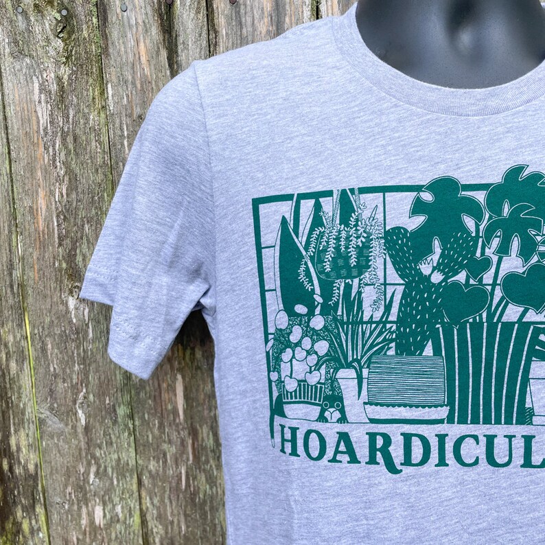 K&ouml;nnte beinhalten: Ein graues T-Shirt mit einem gr&uuml;nen Aufdruck einer Sammlung von Topfpflanzen und dem Text "HOARDICULTURE".