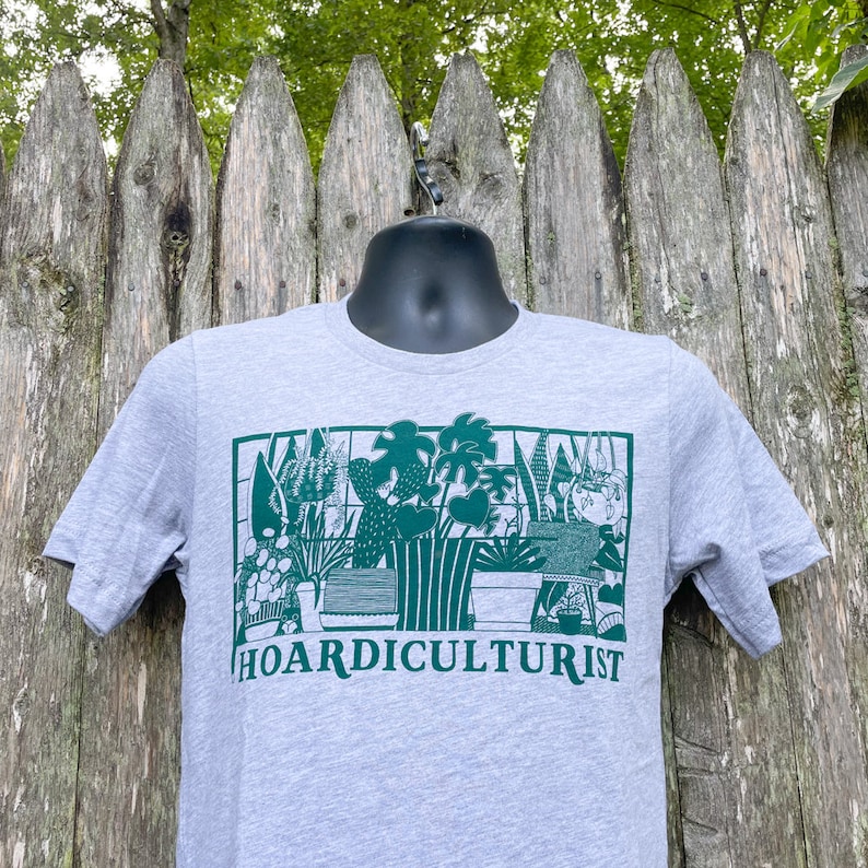 K&ouml;nnte beinhalten: Ein graues T-Shirt mit einer gr&uuml;nen Grafik einer Sammlung von Topfpflanzen. Der Text "HOARDICULTURIST" ist unter der Grafik gedruckt.