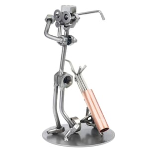 May include: A metal sculpture of a golfer holding a golf club. The sculpture is made of nuts, bolts, and other metal pieces. The golfer is standing on a metal base. The golf club is made of copper.