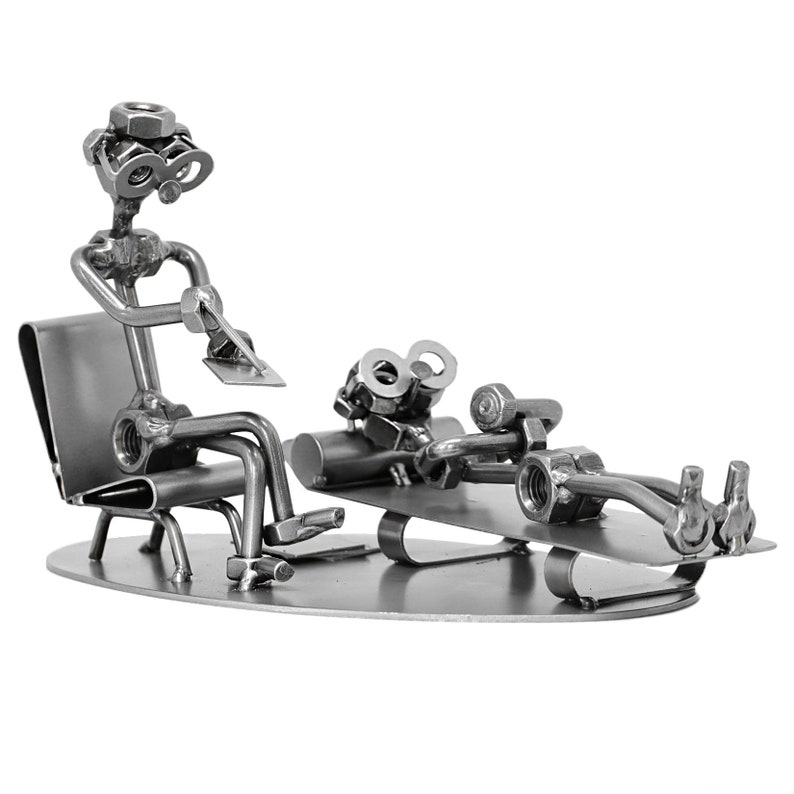 K&ouml;nnte beinhalten: Eine Metallskulptur eines Therapeuten, der auf einem Stuhl sitzt, und eines Patienten, der auf einer Couch liegt. Beide Figuren bestehen aus Muttern, Schrauben und anderen Metallteilen.
