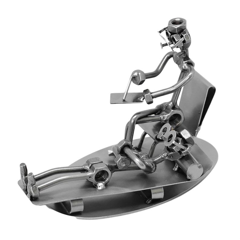 K&ouml;nnte beinhalten: Eine Metallsculptur einer Person, die auf einem Stuhl sitzt und die Beine ausgestreckt hat. Die Skulptur besteht aus Muttern, Schrauben und anderen Metallteilen. Die Person tr&auml;gt eine Brille und h&auml;lt ein Werkzeug in der Hand.