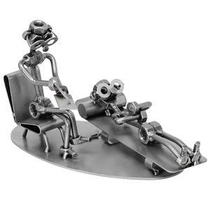K&ouml;nnte beinhalten: Eine Metallskulptur eines Therapeuten und eines Patienten. Der Therapeut sitzt auf einem Stuhl und h&auml;lt eine Klemmbrett. Der Patient liegt auf einer Couch. Beide Figuren sind aus Muttern, Schrauben und anderen Metallteilen gefertigt.