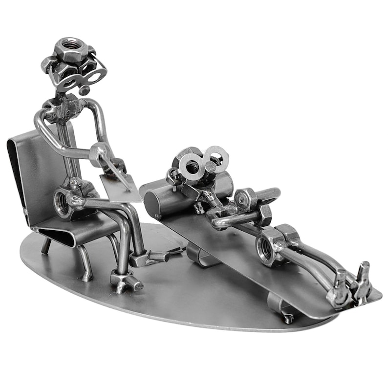 K&ouml;nnte beinhalten: Eine Metallskulptur eines Therapeuten und eines Patienten. Der Therapeut sitzt auf einem Stuhl und h&auml;lt eine Klemmbrett. Der Patient liegt auf einer Couch. Beide Figuren sind aus Muttern, Schrauben und anderen Metallteilen gefertigt.