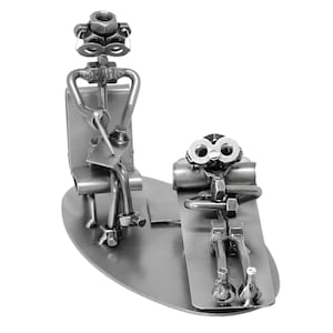 K&ouml;nnte beinhalten: Eine Metallskulptur, die einen Therapeuten zeigt, der auf einem Stuhl sitzt, und einen Patienten, der auf einer Couch liegt. Beide Figuren sind aus Muttern, Schrauben und anderen Metallteilen gefertigt.