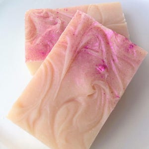 May include: Two bars of handmade soap with a swirl design and pink glitter. The soap is a light beige color.