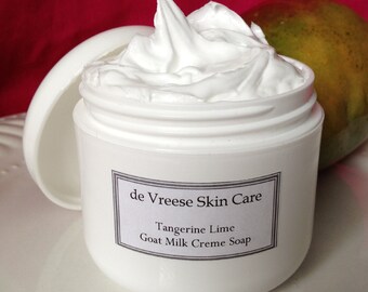 May include: A white jar of de Vreese Skin Care Tangerine Lime Goat Milk Creme Soap. The jar is open and the cream is visible. The jar is sitting on a white surface.