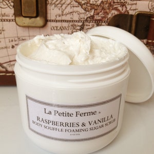 May include: A white jar with a white lid containing a white body scrub. The jar has a black label with the text "La Petite Ferme, k" and "RASPBERRIES & VANILLA BODY SOUFFLE FOAMING SUGAR SCRUB 4 OZ VOL".