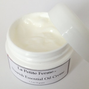 May include: A white jar with a white lid partially open, revealing a white cream inside. The jar is labeled "La Petite Ferme, LLC Nourish Essential Oil Creme 1.2 oz/35 grams."