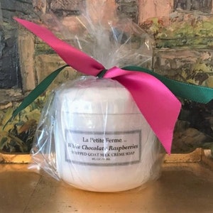 May include: A white jar of whipped goat milk creme soap with a pink and green ribbon tied around it. The jar is labeled "La Petite Ferme White Chocolate Raspberries Whipped Goat Milk Creme Soap 8 fl oz / 236 ml".