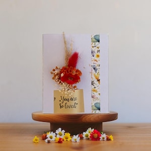 Elegante biglietto di auguri "Sei così amato" con fiori secchi arancioni e rossi, bouquet di fiori secchi.