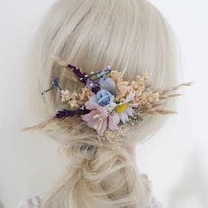 Könnte beinhalten: Ein Blumenhaar kamm mit getrockneten Blumen in Blautönen, Rosa, Lila und Creme. Der Kamm ist aus getrockneten Blumen und Gräsern gefertigt und perfekt, um jeder Frisur einen Hauch von Verspieltheit zu verleihen.