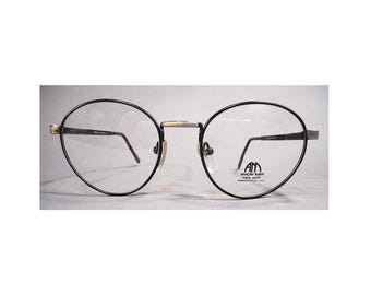 Peut inclure: Lunettes ovales noires avec un pont et des branches dorées. Les montures ont un design fin en forme de fil. Les verres sont transparents. La marque "American Made New York" est visible sur la lentille droite.