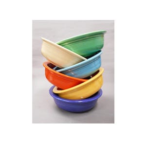 May include: A stack of six round ceramic bowls in various colors including green, cream, light blue, orange, yellow, and purple. Each bowl features a series of concentric circular ridges along the exterior side, creating a uniform, ribbed texture.