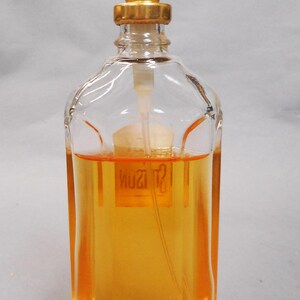 Puede incluir: Un frasco de perfume de vidrio transparente con forma rectangular y tap&oacute;n dorado. El frasco contiene un l&iacute;quido de color dorado. Tiene un pulverizador de pl&aacute;stico blanco y un collar dorado.