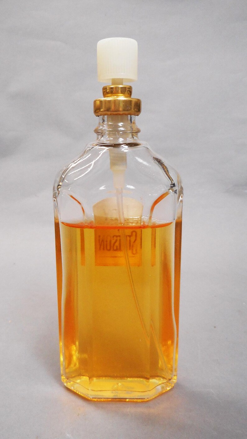 Puede incluir: Un frasco de perfume de vidrio transparente con forma rectangular y tap&oacute;n dorado. El frasco contiene un l&iacute;quido de color dorado. Tiene un pulverizador de pl&aacute;stico blanco y un collar dorado.