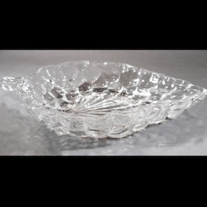 May include: Clear glass leaf-shaped dish with a textured surface. The dish has a scalloped edge and a detailed, bubble-like pattern. The dish is designed for serving or display.