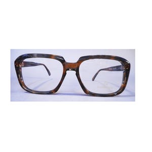 May include: Eyeglasses with a brown and black tortoiseshell pattern frame. The square frames have a thick, bold design with clear lenses and thin metal arms. The glasses are set against a light blue background.