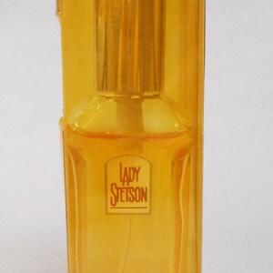 Op de afbeelding: Een fles Lady Stetson parfum in een heldere, geel getinte rechthoekige fles, verpakt in een bijpassende gele plastic doos. Het etiket op de fles luidt "Lady Stetson".