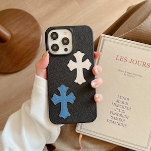 May include: Black phone case with a textured leather finish. The case has two cross-shaped designs, one white and one blue.