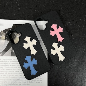 May include: Two black phone cases with cross designs. One case has a white and blue cross, the other has a pink and white cross. The cases are made of a textured material.
