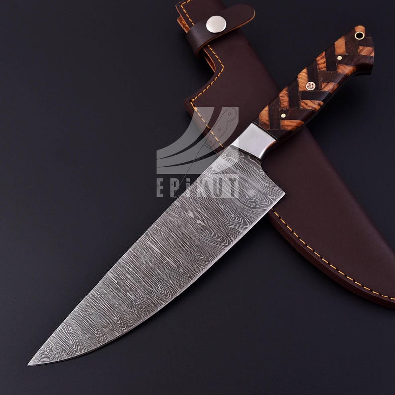 May include: A Damascus steel chef's knife with a wooden handle and a leather sheath. The blade has a wavy pattern and the handle is made of dark wood with a geometric pattern.