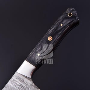 May include: Close-up of the handle of a black and silver kitchen knife with a wood handle. The handle has gold accents and the text "EPIKUT" is visible.