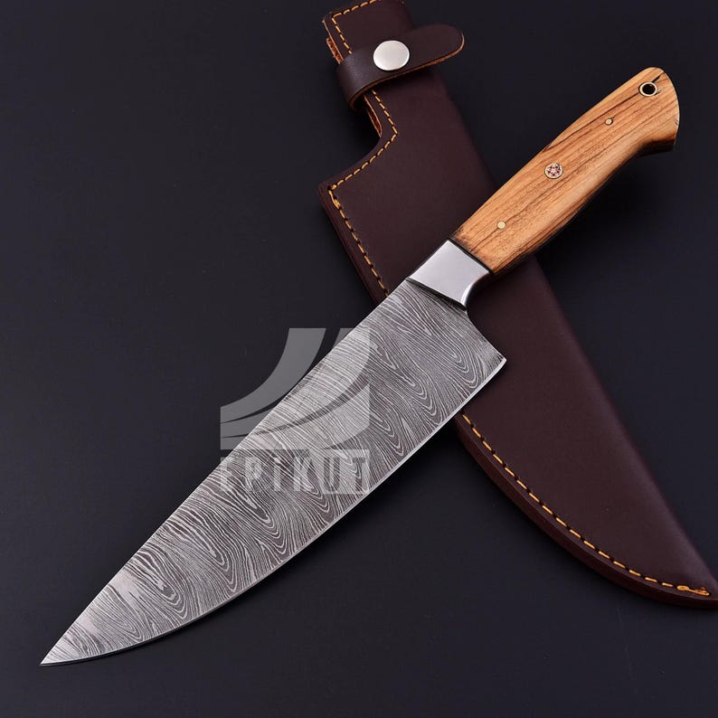 May include: A Damascus steel chef's knife with a wooden handle and a leather sheath. The blade has a wavy pattern and the handle is made of light brown wood.