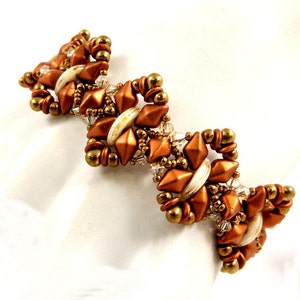 May include: A handcrafted bracelet featuring a zig-zag design. The bracelet is composed of copper-colored, diamond-shaped beads, gold-colored round beads, and small clear crystal beads. White, oblong beads are interspersed throughout the design.
