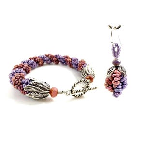 May include: A purple and pink beaded bracelet with a silver clasp and matching earrings. The bracelet is twisted and the earrings are shaped like a cluster of grapes.