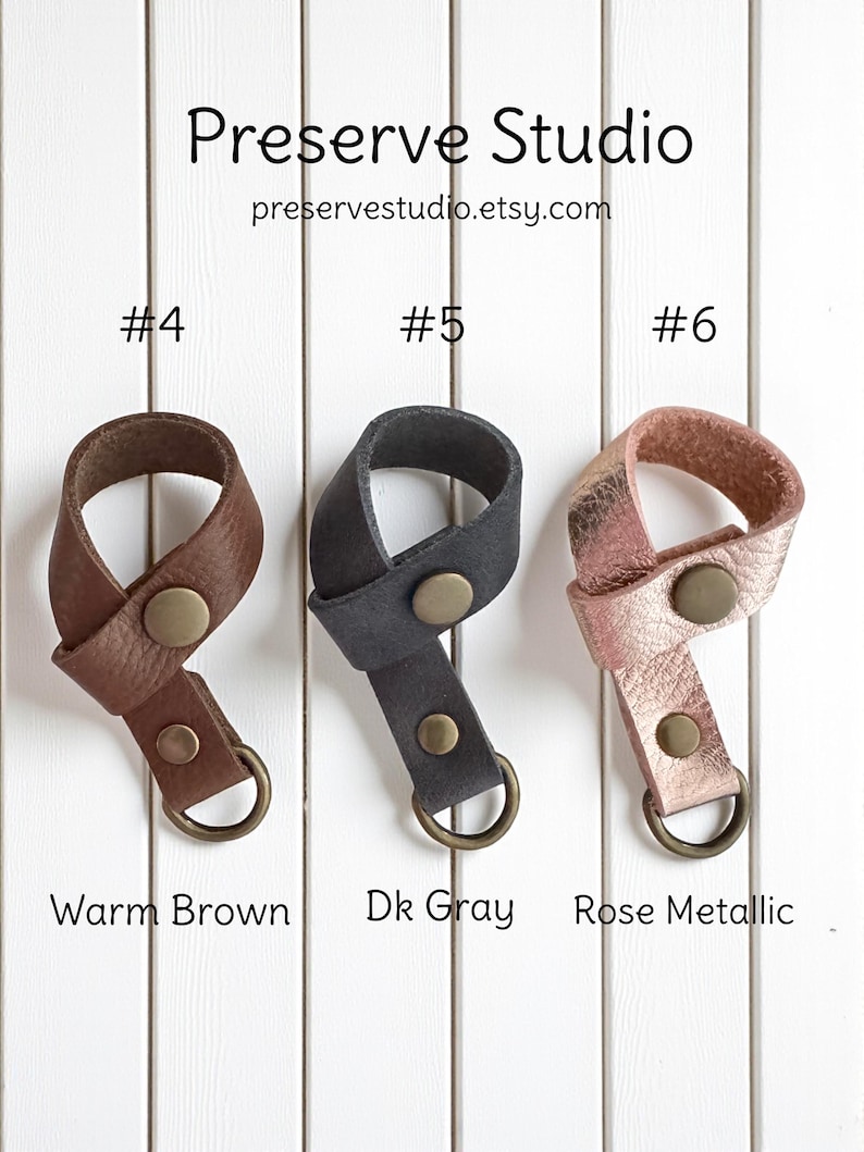 May include: Three leather keychains in warm brown, dark gray, and rose metallic. Each keychain has a metal button and a metal ring. The text "Preserve Studio" and the Etsy website address are at the top.