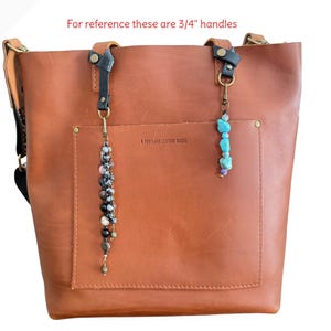 May include: A brown leather tote bag with a front pocket and two decorative beaded charms. The text "Regular" and "Petite" are above the bag. The text "For reference these are 3/4" handles" is also visible.
