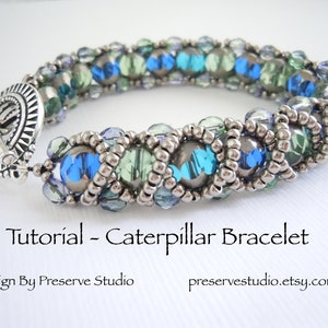 May include: A silver and blue beaded bracelet with a toggle clasp. The bracelet is made with small silver beads and larger blue, green, and clear beads. The bracelet is called a "Caterpillar Bracelet" and is a design by Preserve Studio.