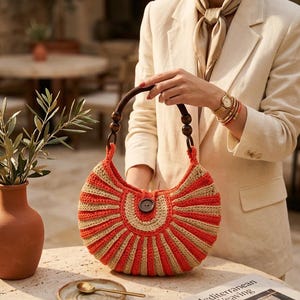 Peut inclure: Un sac à main en crochet en forme de croissant avec des rayures verticales alternées de fil orange vif et beige. Le sac comprend une anse en bois brun foncé avec des perles sphériques et une fermeture à bouton brun foncé au centre.