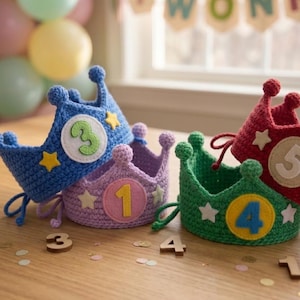 Peut inclure: Quatre couronnes crochetées en bleu, violet, vert et rouge, chacune dotée d'un écusson circulaire avec un chiffre et de petites étoiles appliquées. La couronne bleue affiche le chiffre 3, la violette le 1, la verte le 4 et la rouge le 5.