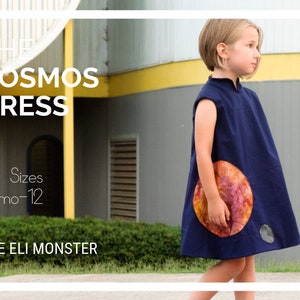 Może przedstawiać: Młoda osoba w granatowej sukience z kolorowym wzorem planety. Sukienka nazywa się "The Kosmos Dress" i jest dostępna w rozmiarach 6 miesięcy-12 lat. Tekst "The Eli Monster" jest również widoczny na zdjęciu.