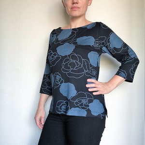 May include: A woman wearing a blue and black floral print top with 3/4 sleeves. The top has a boat neck and a relaxed fit. She is wearing black jeans.
