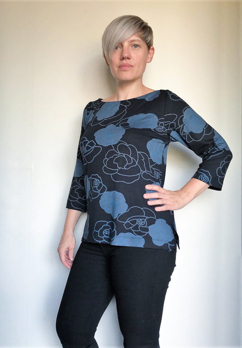May include: A woman wearing a blue and black floral print top with 3/4 sleeves. The top has a boat neck and a relaxed fit. She is wearing black jeans.