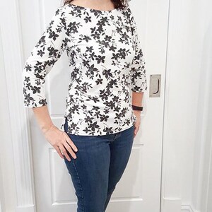May include: A woman wearing a white and black floral print top with 3/4 sleeves and blue jeans.