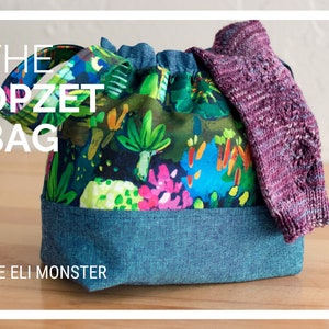 May include: A drawstring bag with a floral print and a denim bottom. The bag has a handle and is filled with a purple knitted sock. The text "THE OPZET BAG" and "THE ELI MONSTER" is printed on the bag.