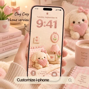Pode incluir: Um smartphone exibindo um papel de parede digital com uma estética rosa suave. A tela apresenta um filhote de pelúcia segurando um coração, uma tulipa em uma moldura, uma luminária e um calendário. O texto diz Clay Cozy theme version e Customize i-phone.