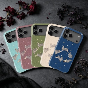 Könnte beinhalten: Fünf Smartphone-Hüllen in Hellblau, Mauve, Olivgrün, Creme und Marineblau. Jede Hülle zeigt ein wiederkehrendes Muster aus kleinen grauen Kaninchen und winzigen weißen Sternen. Die Hüllen haben einen Dreifach-Kameraausschnitt und eine matte Oberfläche.