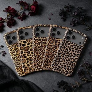 Peut inclure: Cinq coques de smartphone disposées en éventail, chacune présentant un motif léopard distinct avec des nuances variées de brun, de beige et de taches noires. Chaque coque possède une découpe pour un triple objectif photo en haut à gauche.