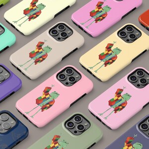 Op de afbeelding: Een verzameling telefoonhoesjes met een cartoon kikker die een kleurrijke trui draagt. De hoesjes zijn verkrijgbaar in verschillende kleuren, waaronder roze, blauw, groen en geel.