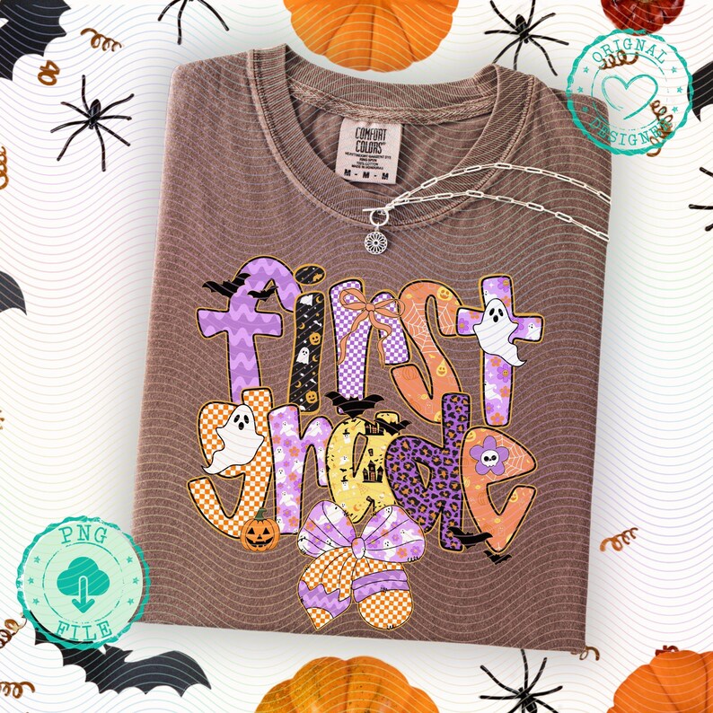 K&ouml;nnte beinhalten: Ein braunes Comfort Colors T-Shirt mit dem Schriftzug "First Grade" in einem farbenfrohen Halloween-Design. Das Design umfasst Geister, Flederm&auml;use, K&uuml;rbisse und eine Schleife. Eine silberne Halskette mit Anh&auml;nger befindet sich auf dem Shirt.