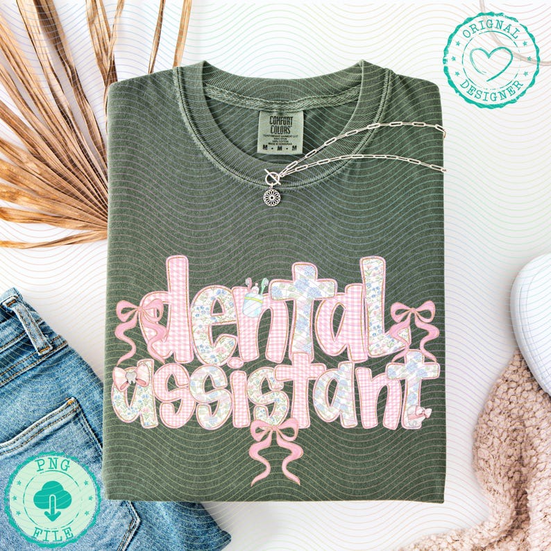 K&ouml;nnte beinhalten: Olivgr&uuml;nes T-Shirt mit dem Schriftzug "dental assistant" in einem rosa und floralen Design. Das Shirt hat eine silberne Halskette mit Anh&auml;nger. Ein PNG-Dateilogo befindet sich in der unteren linken Ecke.
